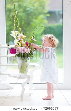 Portrait of a beautiful baby girl playing with fresh flowers wearing a white dress