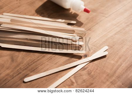 Educative craft. Popsicle sticks and bottle of white glue on wooden workdesk.