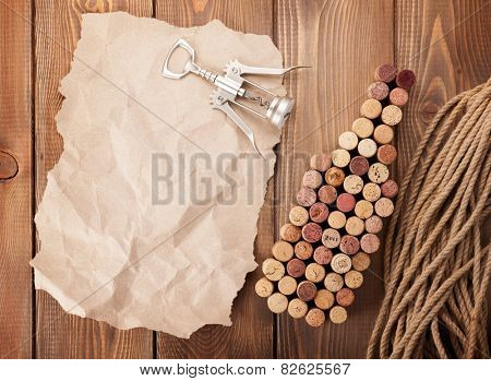 Wine bottle shaped corks, corkscrew and piece of paper for copy space over rustic wooden table background. Top view