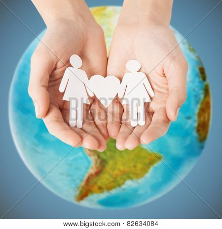 homosexuality, people, love and tolerance concept - close up of female hands holding female gay couple paper figures with heart shape over earth globe and blue background