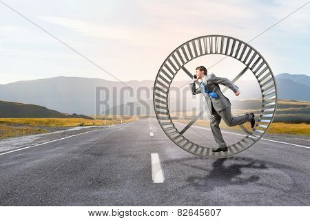 Young businessman running in huge hamster wheel
