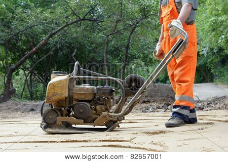 Worker in orange overalls with a plate compactor