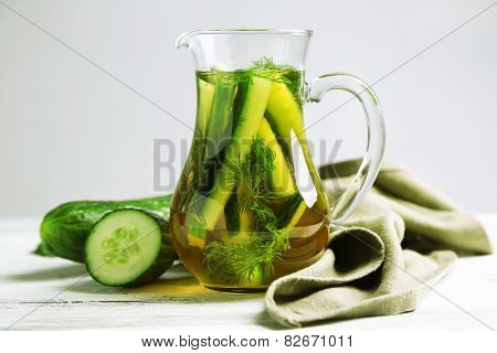 Glass ewer with fresh organic cucumber water on wooden table, on grey background