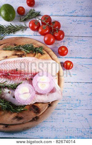 Pangasius fillet with herb, spices and vegetables on cutting board and color wooden table background