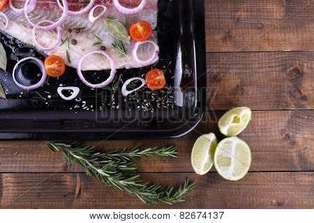 Pangasius fillet with spices and vegetables on firepan and wooden table background