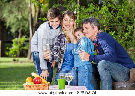 Happy family taking selfportrait through smartphone at campsite
