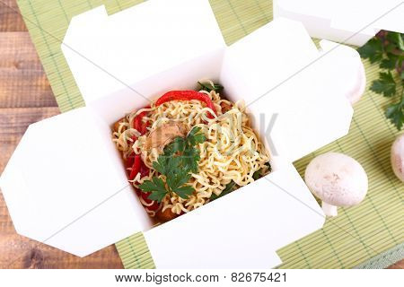 Chinese noodles in takeaway box on mat background