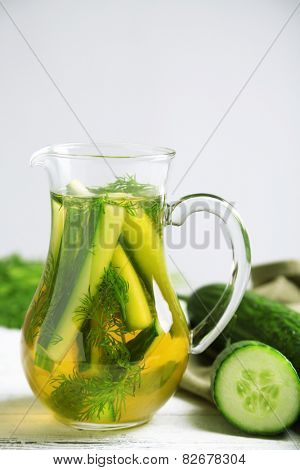 Glass ewer with fresh organic cucumber water on wooden table, on grey background