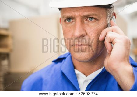 Worker in hard hat using mobile phone in the warehouse