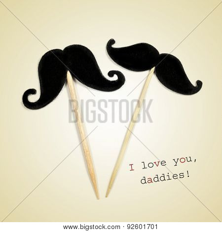 the text I love you daddies and two moustaches glued to wooden toothpicks on a beige background
