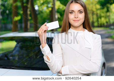 Young woman standing near car and showing card