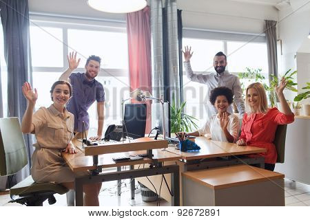 business, startup and office concept - happy creative team waving hands in office