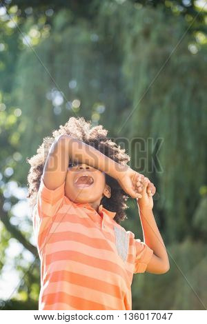 Cute mixed-race boy smiling and hiding behind his arms on a park