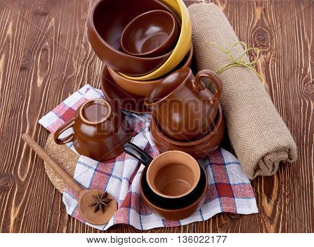 Stack of crockery on wooden table with anise and linen dish-cloth. Set of pottery kitchenware. Buffet, restaurant equipment. Empty plates and cups.