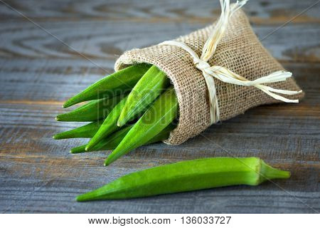 A heap of raw okra or Lady's fingers or gumbo in a bag on wooden background