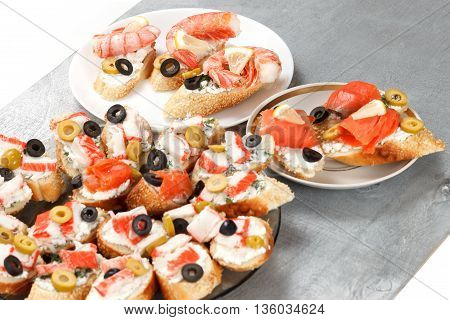 Tasty various italian sandwiches with seafood against rustic wooden background. Crostini with cheese shrimps mussels red fish crab sticks lemon sliced olives on different plates close up with selective focus