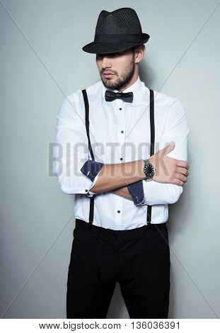 handsome young man in white dress shirt wearing hat, bow tie and suspenders
