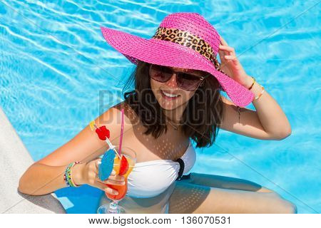 woman in a hat enjoying cocktail in a swimming pool