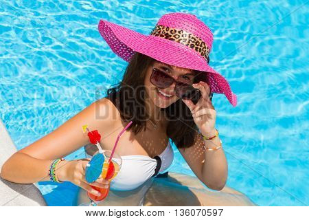 woman in a hat enjoying cocktail in a swimming pool
