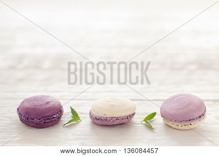 French purple macaroons horizontal line copyspace. Sweet macaroons put in hirizontal line in downside of pictire on white wooden background. Macaroons line decoratrd with mint