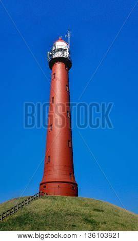 The red-brown painted round cast iron High Lighthouse near the Dutch seaport of IJmuiden is built on a hill in 1878 and 35 meters high. It is a sunny fday in the summer season.