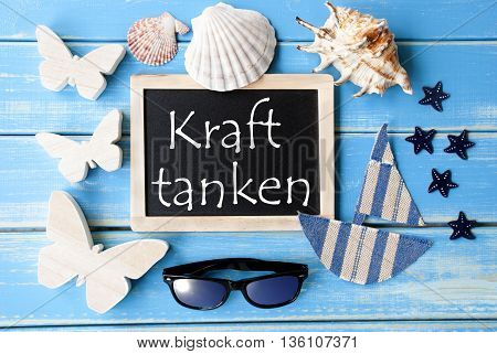Flat Lay Of Chalkboard On Blue Wooden Background. Nautical Summer Decoration As Holiday Greeting Card. German Text Kraft Tanken Means Relax