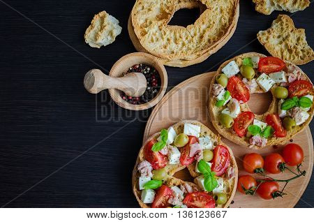 Italian appetizer Friselle. Italian dried bread Friselle with tomatoes cherry cheese mozzarella olives tuna basil and pepper in wooden pounder. Italian food. Healthy vegetarian food. Top view.
