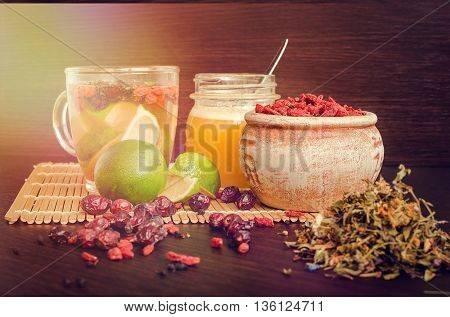 Still life glass cup of herbal tea with lime honey goji berries sweetbrier and blueberry on wooden background. Healthy food. Alternative medicine. Selective focus.