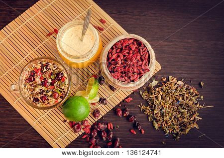 Still life glass cup of herbal tea with lime honey goji berries sweetbrier and blueberry on wooden background. Healthy food. Alternative medicine. Selective focus. Top view.