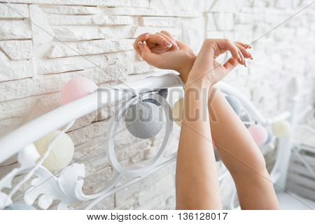 Female hands on bed headboard closeup. Unrecognizable woman hands on forged bed headboard in bedroom. Crossed female hands in bed. Seduction, temptation concept