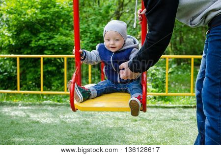 Father swinging his baby. Father and son on a swing in a park. Happy father pushing toddler boy on swing in playground. Smiling little boy sitting on a swing father pushing. Happy family.