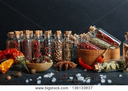 Assorted dry spices in glass bottles on dark background
