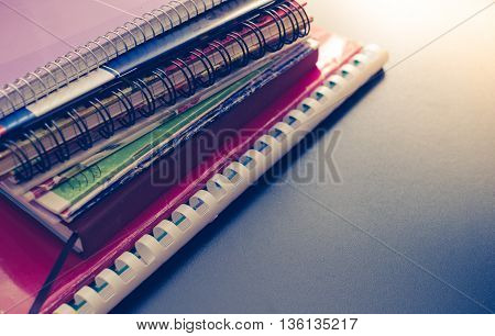 Notebook stack on blackboard background. Back to school concept with space for text. School supplies. Schoolchild and student studies accessories. Back to school concept. Toned image.