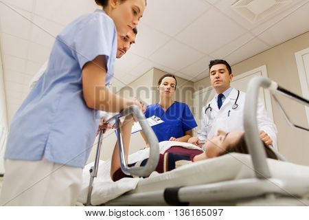 profession, people, health care, reanimation and medicine concept - group of medics or doctors carrying unconscious woman patient on hospital gurney to emergency