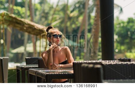Sexy woman in bikini at beach cafe bar. Girl enjoying a cup of coffee outside. Smiling happy Caucasian woman near ocean beach. young beautiful woman relaxing on tropical vacation