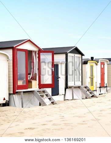 Beach huts or houses and blue sky. Multicolored beach bathing huts with white sand and clear blue sky. Beach scene with copy space. Side view of beach huts in a row.