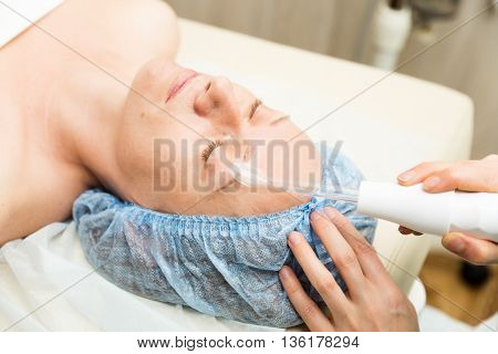 Beautician makes darsonvalization to young woman. The cosmetic procedures for the face. Beauty treatments in the spa salon. Facial Skin Care.