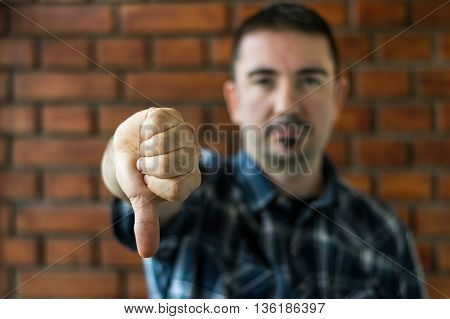 Young man in plaid shirt with trim beard in his 30s showing thumbs down. Selective focus