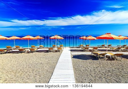 White wooden walkway on beach including umbrellas with deck chairs. Aegean Sea. Greece Rhodes. pebble beach