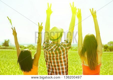 Multiracial friends putting hands up in countryside with back lighting - Multi ethnic young people enjoying sunny day outdoor in nature - Freedom in nature concept - Focus on hat - Vintage filter