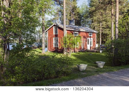 UMEA, SWEDEN ON MAY 28. View of a wooden Falu Red Painted cabin by a lake on May 28, 2013 in Umea, Sweden. Entry, garden and a grove of trees. Editorial use.