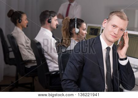 Young male consultant is talking on the phone and his collegues are supervised by manager