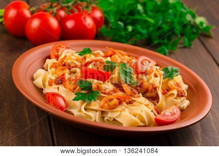 Fettuccine pasta with shrimp tomatoes and herbs. wooden background