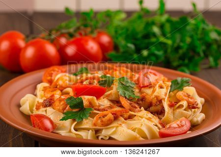 Fettuccine pasta with shrimp tomatoes and herbs. wooden background