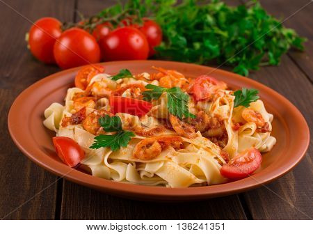 Fettuccine pasta with shrimp tomatoes and herbs. wooden background