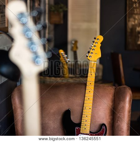 Detail of Electric Guitar Neck Leaning Against Leather Seat. Other Necks in Background and Foreground.