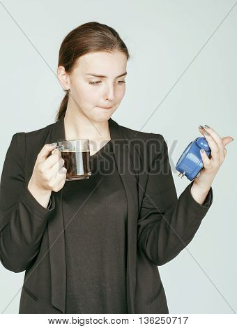 young beauty woman in business style costume waking up for work early morning on white background with clock alarm dreanking coffee close up