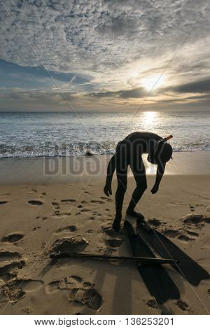A snorkeler with a harpoon standing on a beach at sunset and clouds in the sky in Tarifa, Spain-