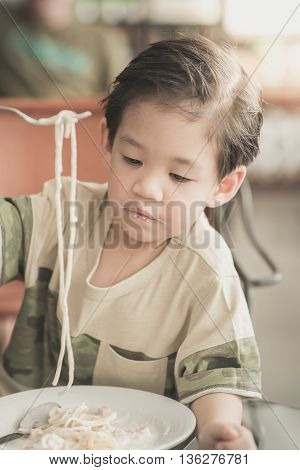 Cute Asian chid eating Spaghetti Carbonara in restaurant vintage fiter