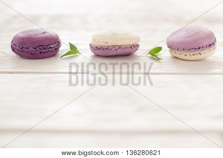 Macaroons line on wooden background copyspace. Three purple french macaroons horizontal line at the top of image. Ratafia on white wooden background